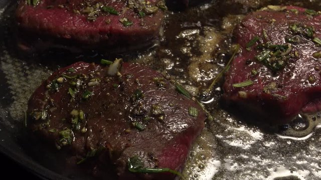 Venison steaks on frying pan. Deer meat sirloin is spiced with garlic, rosemary and thyme.
