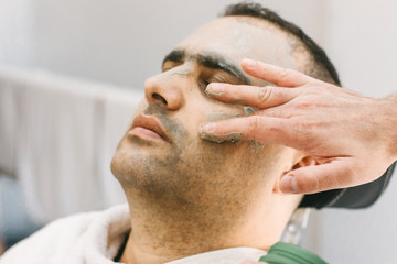 Fototapeta premium Male skin care in a beauty salon. Applying clay cleansing mask on a man's face