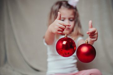 Little baby girl holds red christmas balls. A kid plays with christmas ornamentss on the plaid....