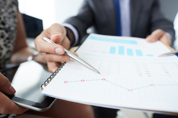 Businessman and woman discussing on stockmarket charts in office. Men in a suit hold a clipboard with financial charts.