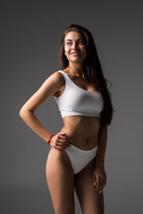 Fototapeta na wymiar Proud of her perfect body. Attractive young brown hair woman in white lingerie posing against grey background and smiling
