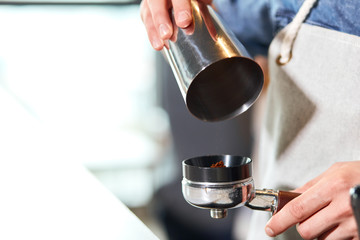 Shining metal coffee pot over tamper, hands prepare aromatic tasty latte or cappuccino for lovely customer in coffee shop, blurred background, close up