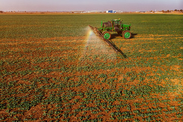 Tractor spraying fertilizer or pesticides on field with sprayer