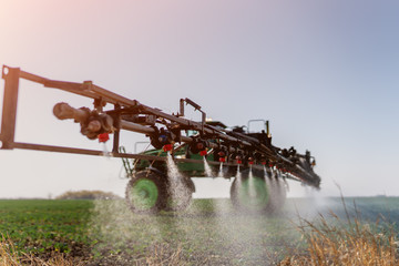 Tractor spraying fertilizer or pesticides on field with sprayer - obrazy, fototapety, plakaty