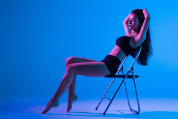 Sexy woman in black underwear sitting on a chair on a black light background.