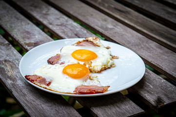Fried eggs with bacon on the wooden table in the garden