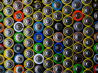 A large number of old AA batteries of different colors. Top view of alkaline batteries.