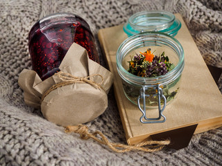 A jar of raspberry jam. Dry useful herbs and a book lie on a woolen blanket. Folk medicine