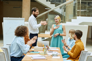 Tall unshaved man together with clevel teamworkers playfully applauds young charming woman with friendly smile in comfortable designers agency