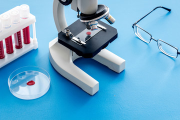 Blood testing laboratory. Samples viewing under microscope near tubes on blue background top view copy space