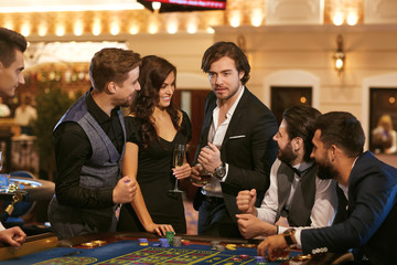 Group happy people make bets gambiling at the roulette table in the casino.