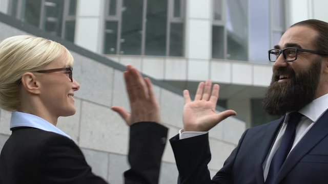 Lady and male in formalwear making high-five gesture, lucrative deal, business