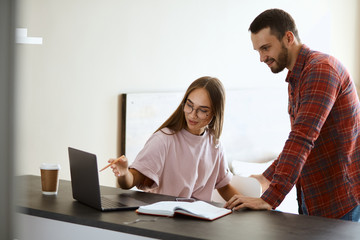 Obraz premium charming playful girlfriend points at screen of laptop computer, showing funny photo, sitting at black wooden table, friendship concept