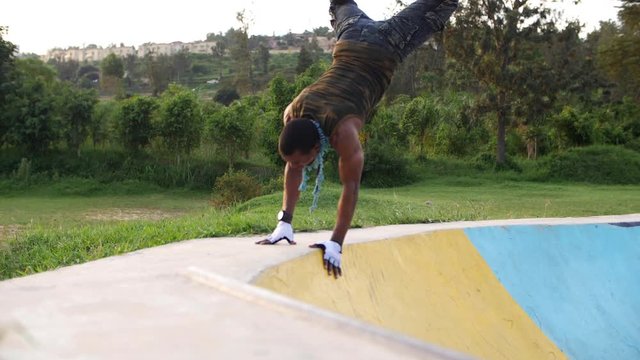 Dexterous young man rollerblader jumping and falling on the ramp with two hands at midday