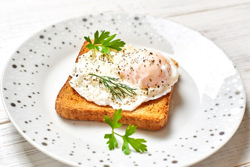 Poached egg, benedict on toasted white bread toast with salad and spices on a plate on a light wooden background.
