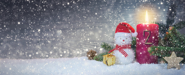 Christmas background with second Advent candle and Snowman with red decoration.