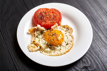 Grilled egg and grilled tomato on a plate on a wooden background. Fast and easy to prepare breakfast.