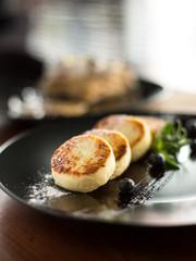 Ukrainian traditional dish cottage cheese pancakes with icing sugar and blueberries, mint, dessert, on the table, restaurant 