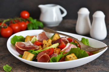 Salad with tomatoes, prosciutto and grilled cheese on a stone background.