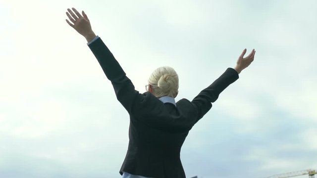 Lady in formalwear celebrating victory and raising hands to sky, successful deal