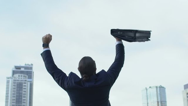 Successful businessman raising hands in winner gesture, profitable deal, sky