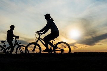Obraz premium Boy and young girl riding bikes in different directions, silhouettes of riding persons at sunset in nature