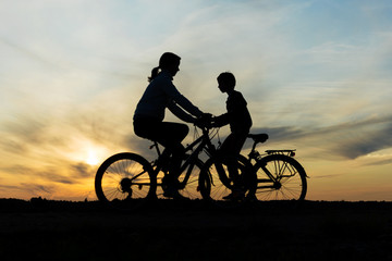 Obraz na płótnie Canvas Boy and young girl riding bikes in different directions, silhouettes of riding persons at sunset in nature
