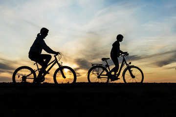Obraz premium Boy and young girl riding bikes in countryside , silhouettes of riding persons at sunset in nature