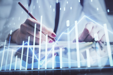 A woman hands writing information about stock market in notepad. Forex chart holograms in front....