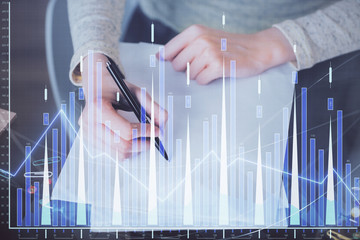 Hand taking notes in notepad. Forex chart holograms in front. Concept of research. Multi exposure