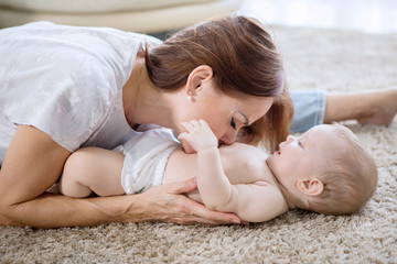 Happy mother kissing belly of her baby girl at home