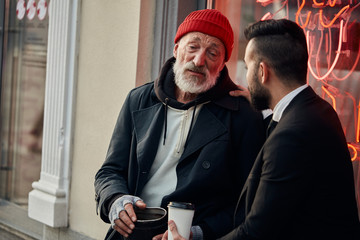 Responsive rich man sat down with homeless man in street and talk, listen to him