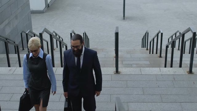 Lady and male partners walking on staircase near office building, cooperation