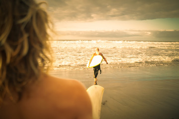 Happy family having fun surfing in the sunrise. Surfer's son waiting for his dad on the shore. Sporty people lifestyle and extreme sport concept - Image