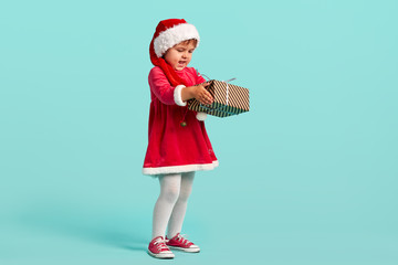 Adorable small baby girl in christmas hat and red dress on the studio background