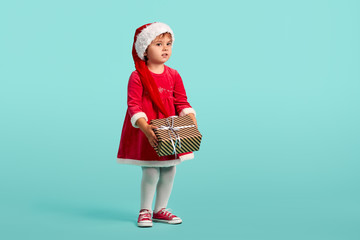 Adorable small baby girl in christmas hat and red dress on the studio background