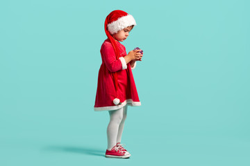 Adorable small baby girl in christmas hat and red dress on the studio background
