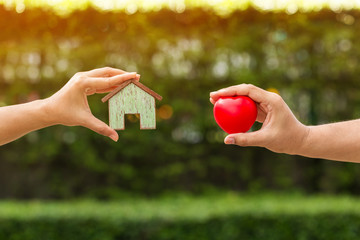 Man and woman hand hold the  home model  and red heart filed together on sunlight in the public park, The buying a new real estate as a gift to family or the one loved concept.