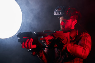 Fototapeta premium Young man holding virtual reality gun, ready to shoot. Studio shoot isolated over ultra violet background