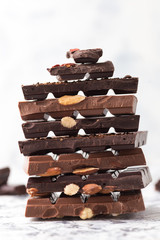 Chocolate tower. Dark and milk chocolate bars with nuts, berries and coffee beans on a grey background