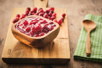Cranberry jam in a wooden bowl on a wooden background.
