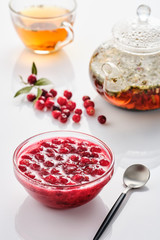 Cranberry jam in a glass bowl and teapot on a white background.