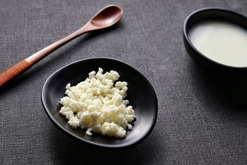 kefir grains and fermented milk in dark dish with bamboo spoon on dark gray background closeup 