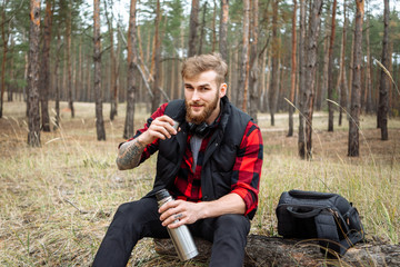 Naklejka na ściany i meble Man resting in the forest and drinking tea from the thermos.