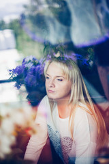 portrait of young blond woman looking through window glass