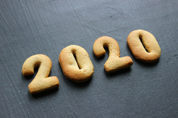 2020 new year background. Baked letters Happy New year and numbers 2020, stars, snowflakes on a black background.Greeting card with gingerbread. Card with New year from gingerbread on a wooden black t