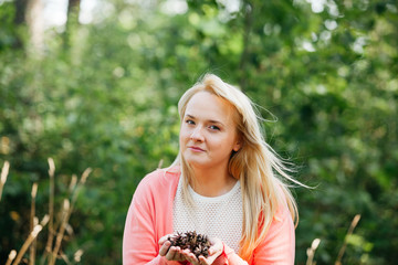 portrait of young woman in the park holding pine cones in hands
