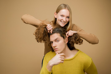 Enjoy twogether. A blonde girlfriend making funny hairstyle to her boyfriend with curly hair. Young...