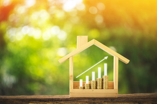 Stacking gold coins with growing interest value put in a wooden home model and bar and arrow graph on bokeh background in the public park, Loan and business investment for real estate concept.