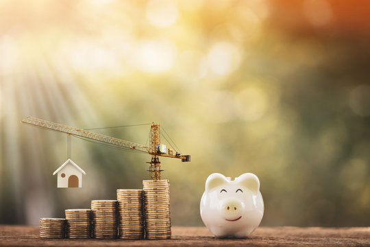 Piggy bank and stacking gold coins with increase and tower crane and hoist brake solutions with build new house in the public park, saving money and loan for construction real estate and home concept.